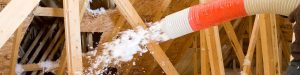 Worker Spraying Blown Fiberglass Insulation Between Attic Trusses